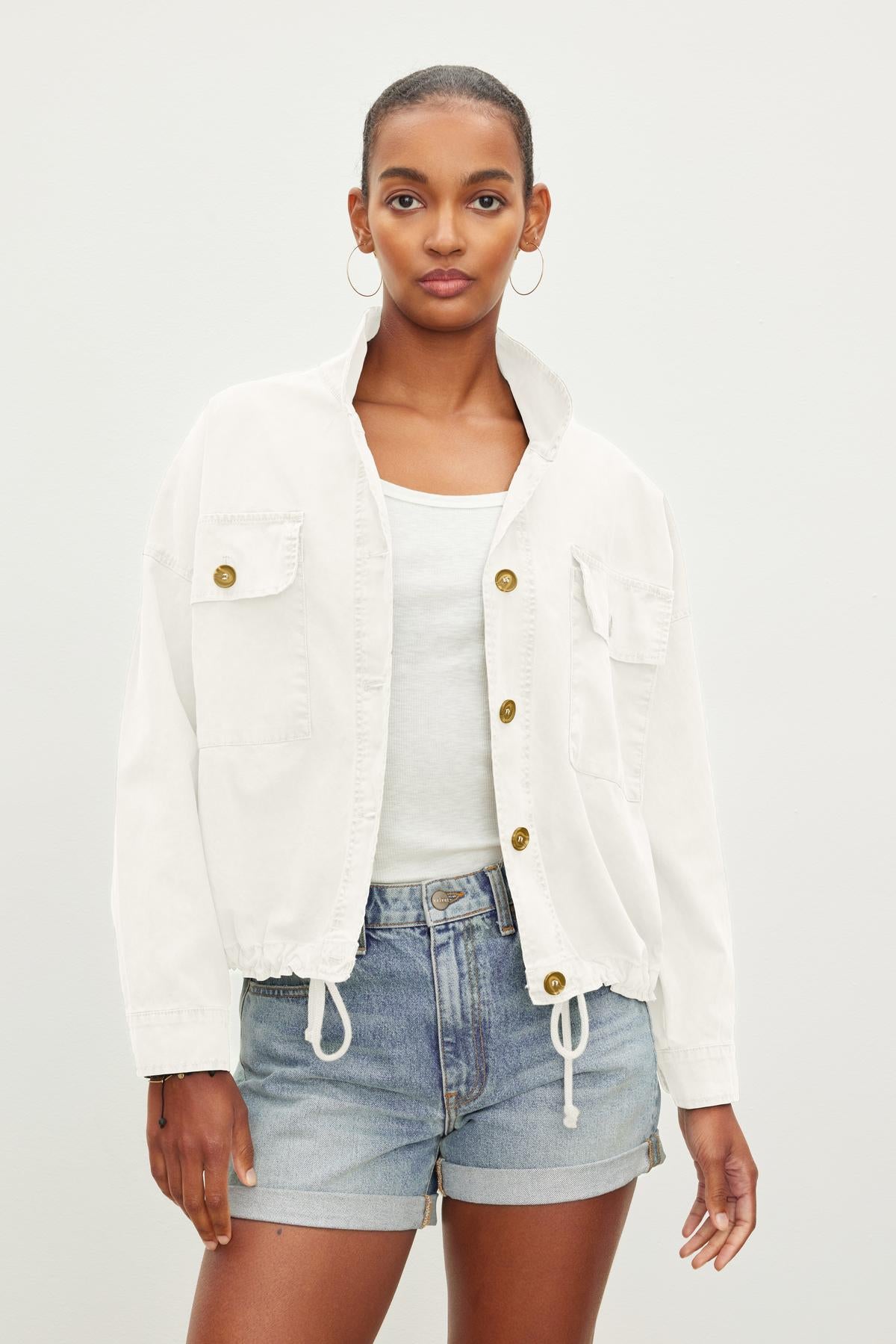 A person with short hair wears a Velvet by Graham & Spencer NICOLA JACKET over a white tank top and blue denim shorts, standing against a plain background.-37229021921473