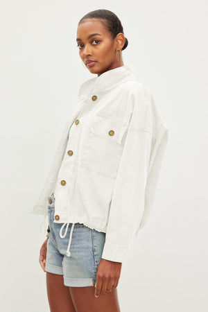 A person wearing a white, NICOLA JACKET by Velvet by Graham & Spencer and denim shorts, standing against a plain background.