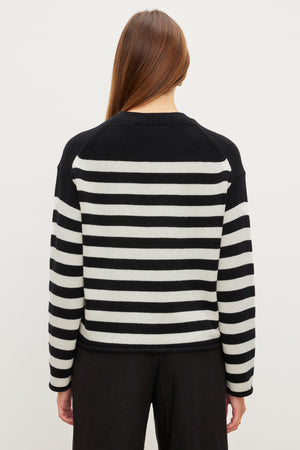 A person with long hair is seen from the back wearing the Velvet by Graham & Spencer LEX COTTON CASHMERE SWEATER, featuring black and white stripes, paired with black pants for a laid-back vibe against a plain background.