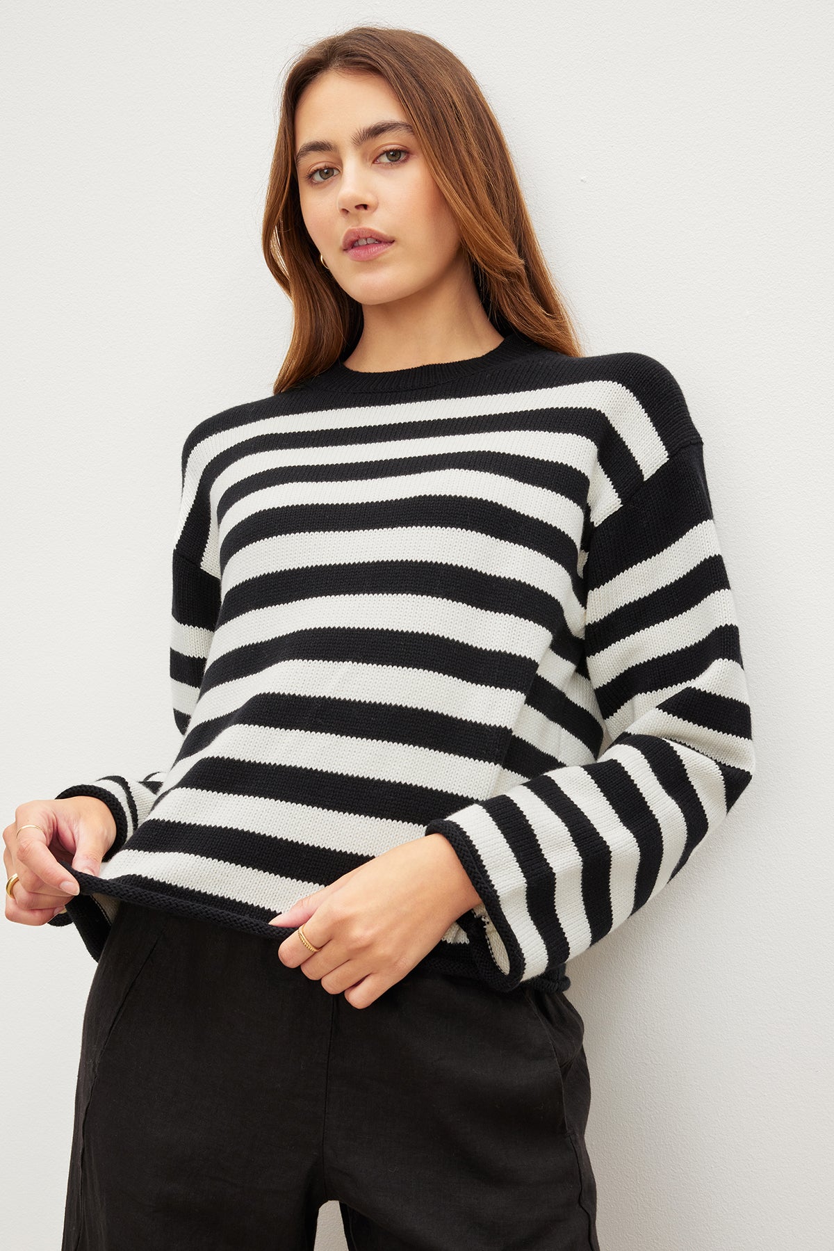 A person wearing the LEX COTTON CASHMERE SWEATER by Velvet by Graham & Spencer pairs its classic Breton stripes with black pants, creating a relaxed vibe against the plain background.-35967621824705