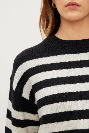 The individual, seen from shoulders to neck, dons a Velvet by Graham & Spencer LEX COTTON CASHMERE SWEATER with black and white stripes in a classic Breton style. Sporting long brown hair and small hoop earrings, they exude a laid-back vibe.