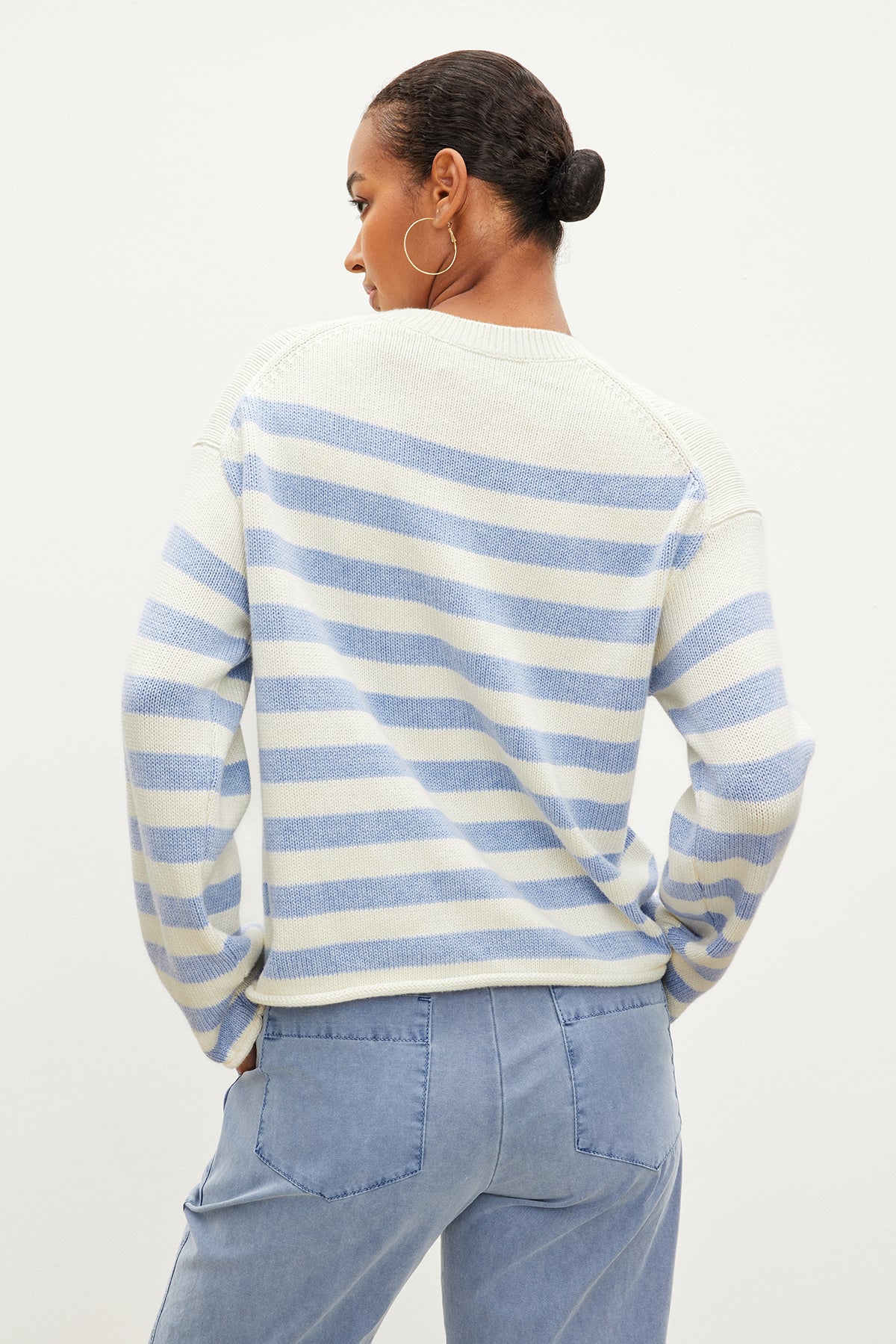 Wearing the Velvet by Graham & Spencer LEX Cotton Cashmere Sweater in blue and white stripes with light blue jeans, a person stands with their back turned, embodying effortless style.-35967621759169