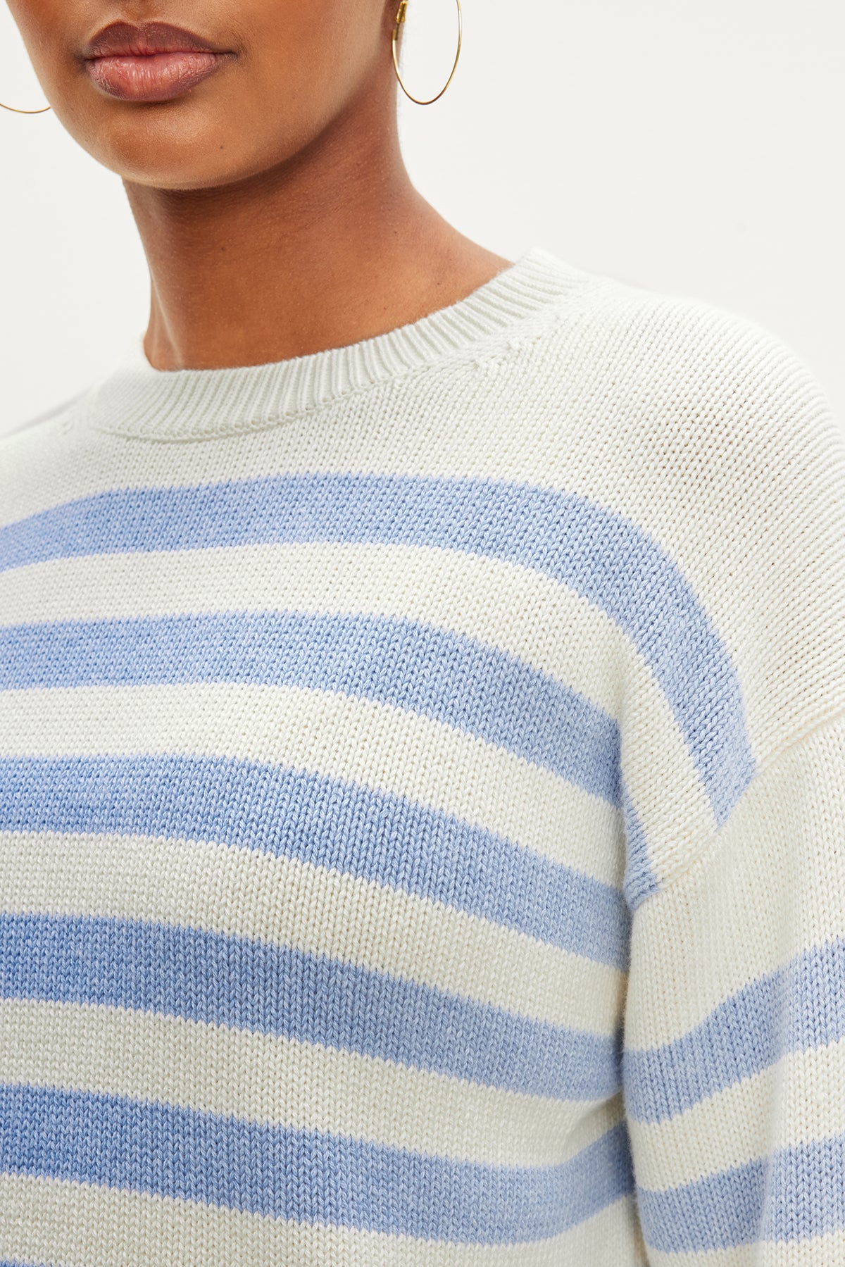 A person wears the LEX COTTON CASHMERE SWEATER by Velvet by Graham & Spencer, featuring a white and light blue striped, classic Breton silhouette paired with gold hoop earrings for a laid-back vibe.