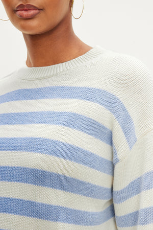 A person wears the LEX COTTON CASHMERE SWEATER by Velvet by Graham & Spencer, featuring a white and light blue striped, classic Breton silhouette paired with gold hoop earrings for a laid-back vibe.