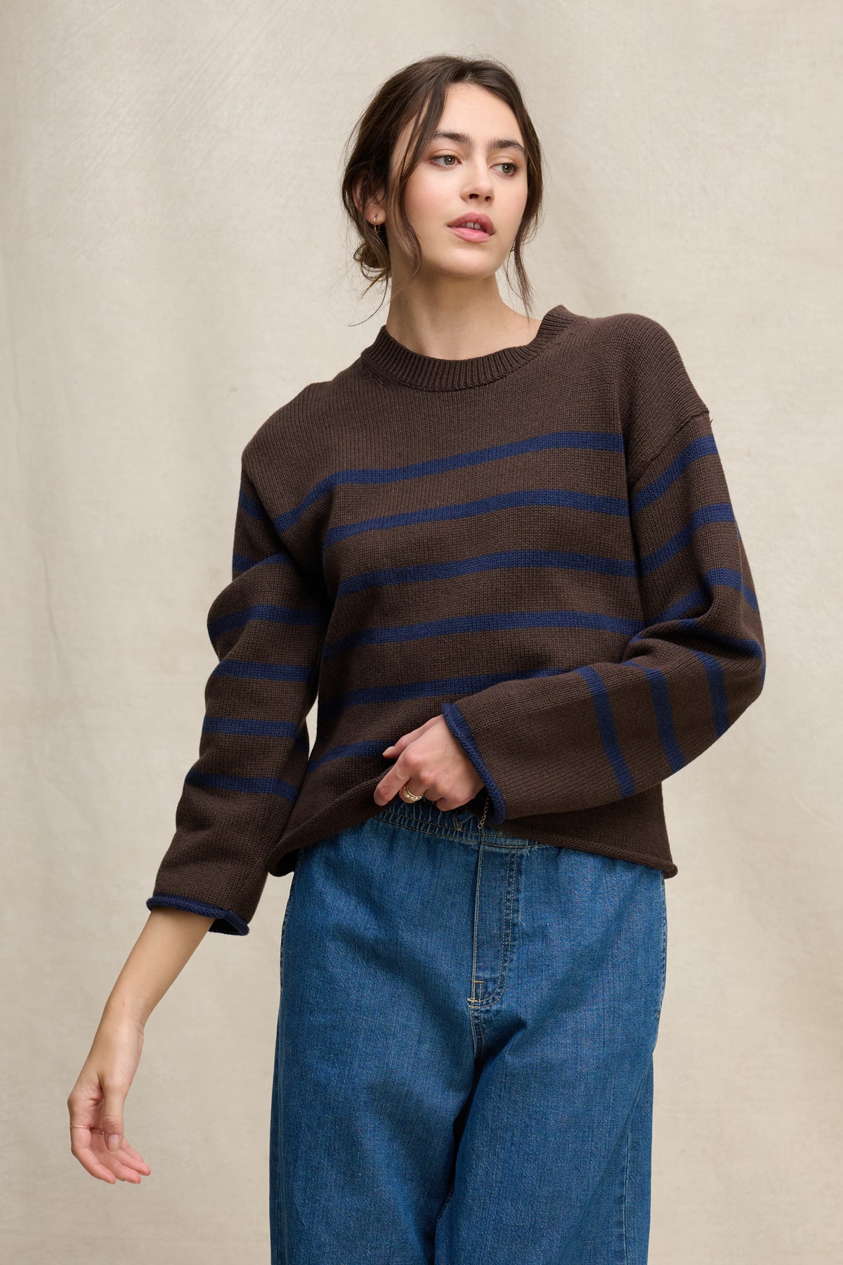A woman wears the Velvet by Graham & Spencer LUCIA SWEATER, a relaxed-fit cotton-cashmere piece with blue horizontal stripes, paired with blue jeans, posing against a neutral background.-39838359584961