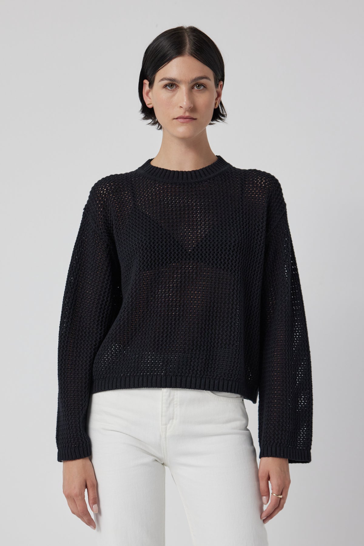 A person with short dark hair is wearing the Velvet by Jenny Graham's KANAN cotton cashmere mesh sweater and white pants, standing against a plain background.