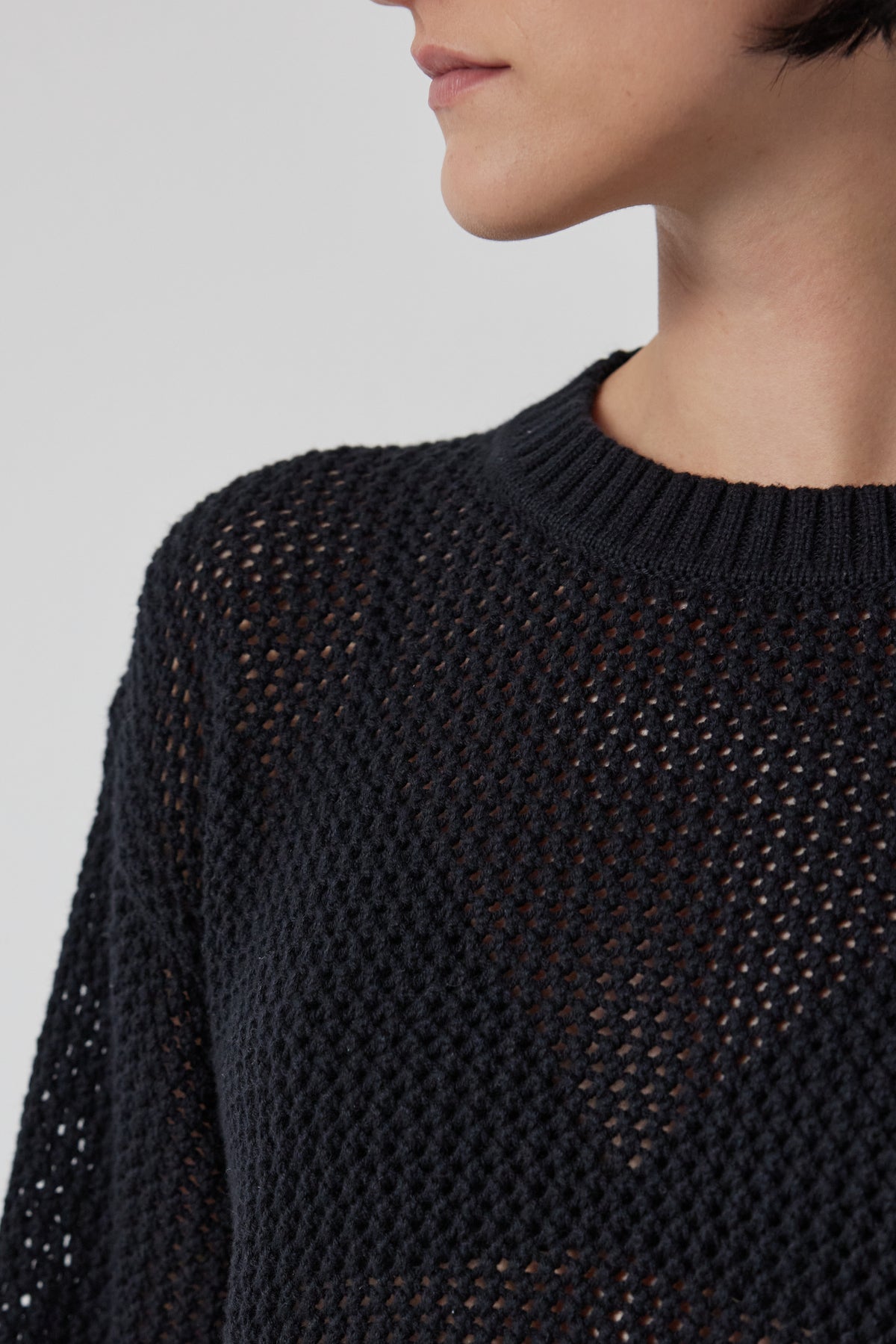 A person wears the KANAN COTTON CASHMERE MESH SWEATER by Velvet by Jenny Graham, in black with a textured knit, facing right with a neutral expression.