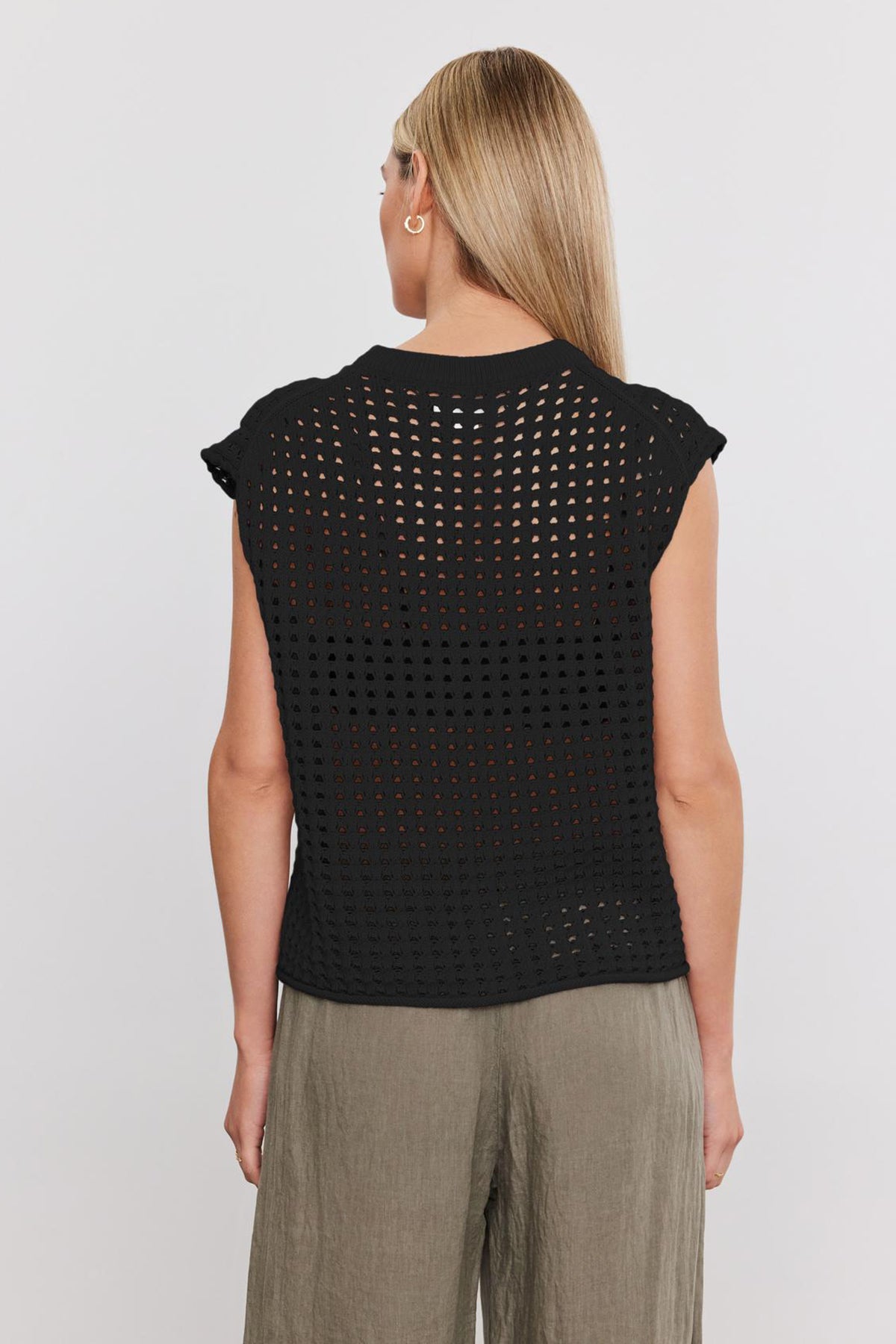 A person with long blonde hair is seen from behind, wearing a black, sleeveless, open-knit Velvet by Graham & Spencer MAISON SWEATER and olive green pants against a plain white background.-37054537924801