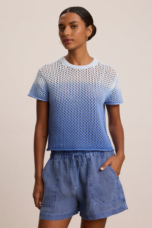 A woman wears the Velvet by Graham & Spencer POPPY Cotton Cashmere Mesh Sweater in blue and white, paired with blue drawstring shorts, standing against a plain background.