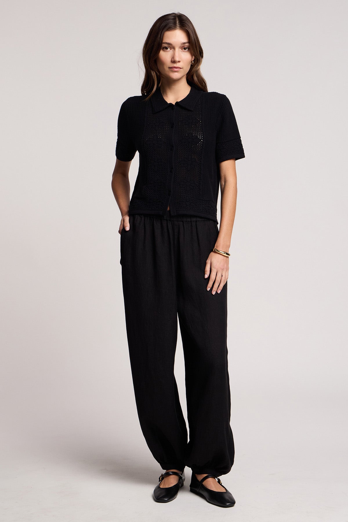 A person stands facing forward, hands in pockets, wearing a short-sleeve black shirt, Velvet by Graham & Spencer CAMBER LINEN PANT with an elastic waist, and black flat shoes against a plain background.-41371565490369
