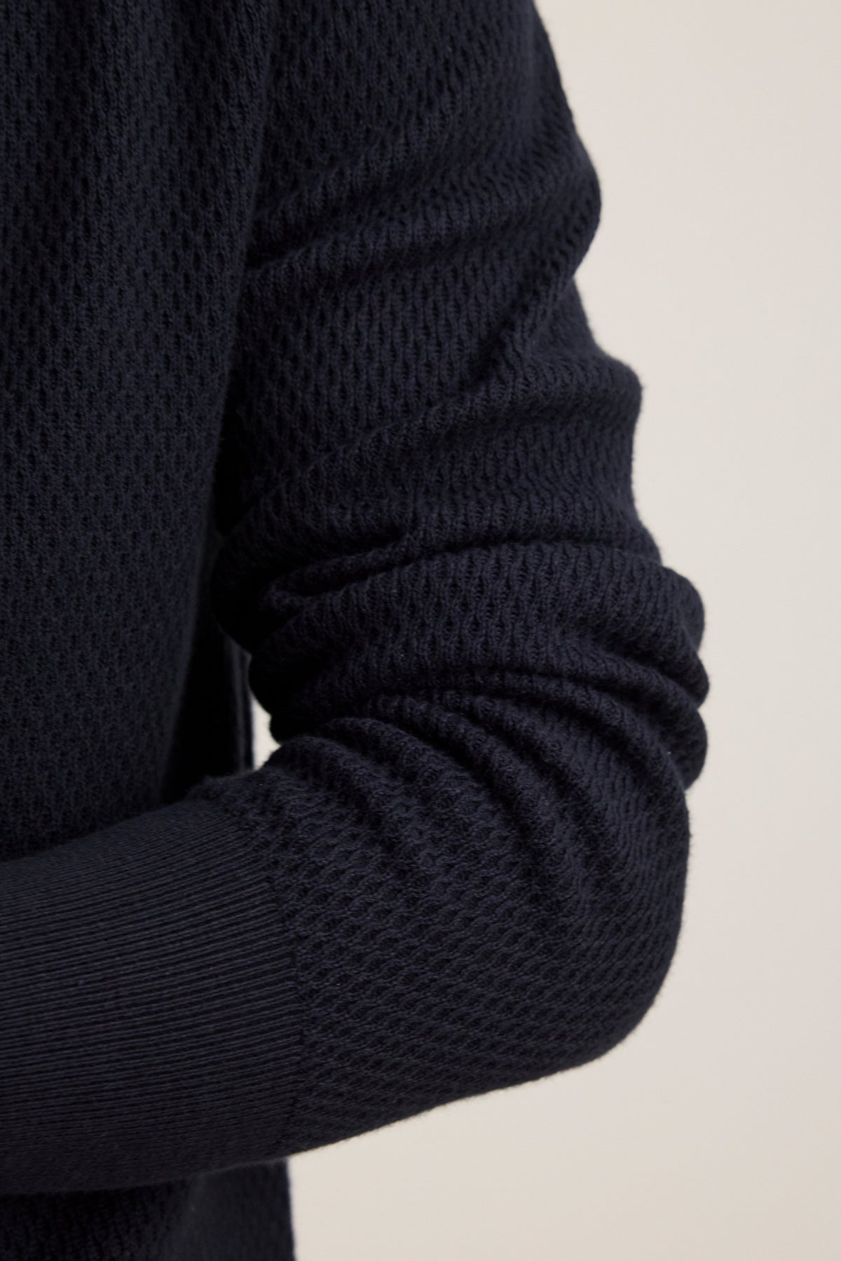 Close-up of a person's arm wearing the THALEN SWEATER POLO by Velvet by Graham & Spencer, featuring a dark textured knit and ribbed cuff, crafted from a soft cotton cashmere blend.