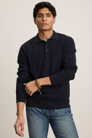 A person wears the THALEN SWEATER POLO by Velvet by Graham & Spencer—a navy textured knit-collar sweater polo—paired with blue jeans, standing facing forward against a plain light background.