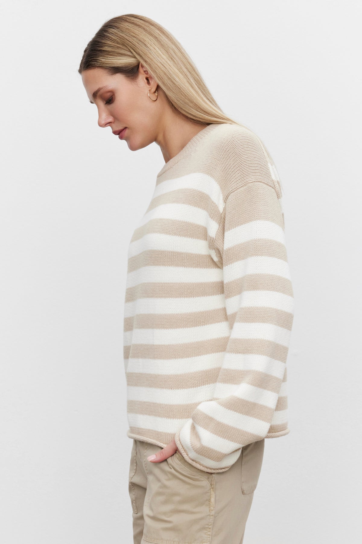 Against a plain white backdrop, a person models the LEX COTTON CASHMERE SWEATER in beige and white stripes by Velvet by Graham & Spencer, paired with beige pants. The luxurious cotton cashmere blend enhances this chic and timeless look.-37676314427585