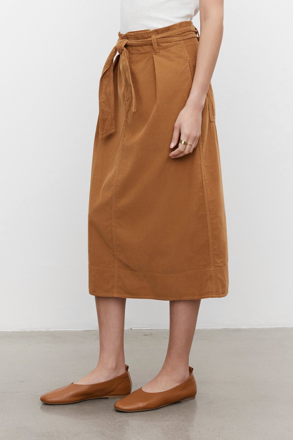 A person wearing a white top and the KENNEDY CORDUROY SKIRT by Velvet by Graham & Spencer, paired with brown flats. Only the lower part of the body is visible.-37856324714689