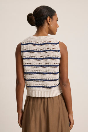A woman with her hair in a bun is seen from the back, wearing the CALISTA SWEATER VEST by Velvet by Graham & Spencer and a brown skirt against a plain background.