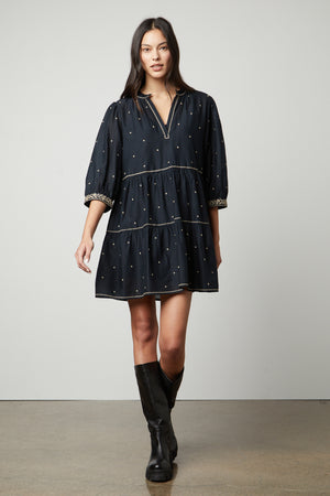 The model is wearing a vintage black dress, the KILEY EMBROIDERED BOHO DRESS by Velvet by Graham & Spencer, with embroidered details.