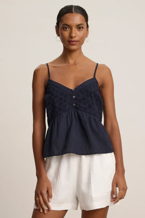 A woman stands facing forward, wearing the ALIAH EYELET TANK TOP by Velvet by Graham & Spencer and white shorts, against a plain light background.