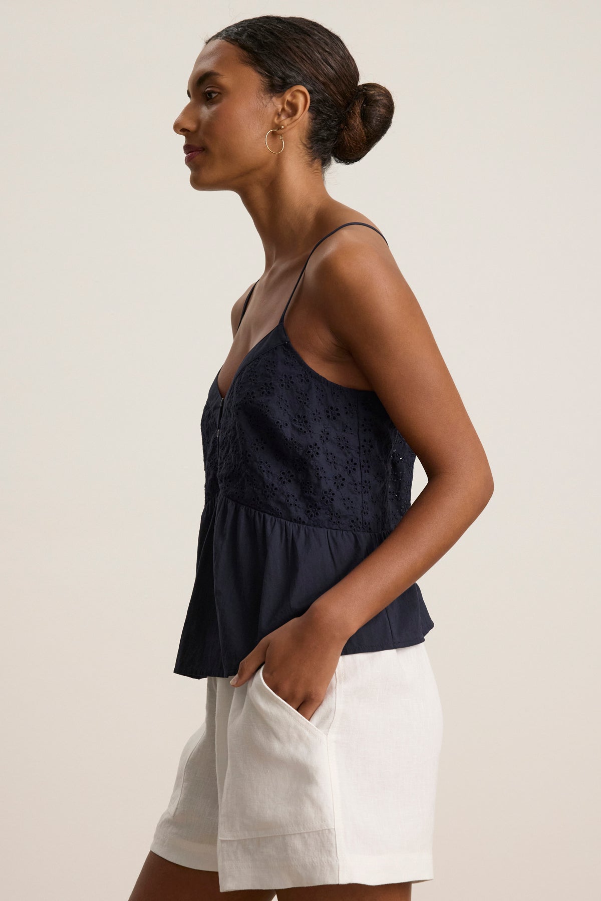 A woman in profile wears the Velvet by Graham & Spencer ALIAH EYELET TANK TOP in navy blue with white shorts against a plain light background.