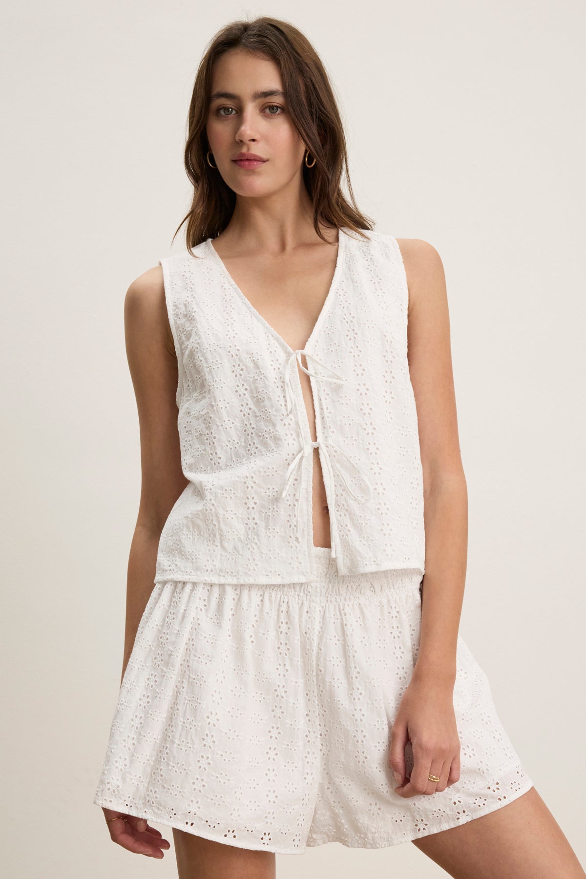 A woman wears the AVA EYELET TOP by Velvet by Graham & Spencer, a cotton sleeveless top with front tie, paired with matching loose shorts, standing against a plain light background.-39123270959297