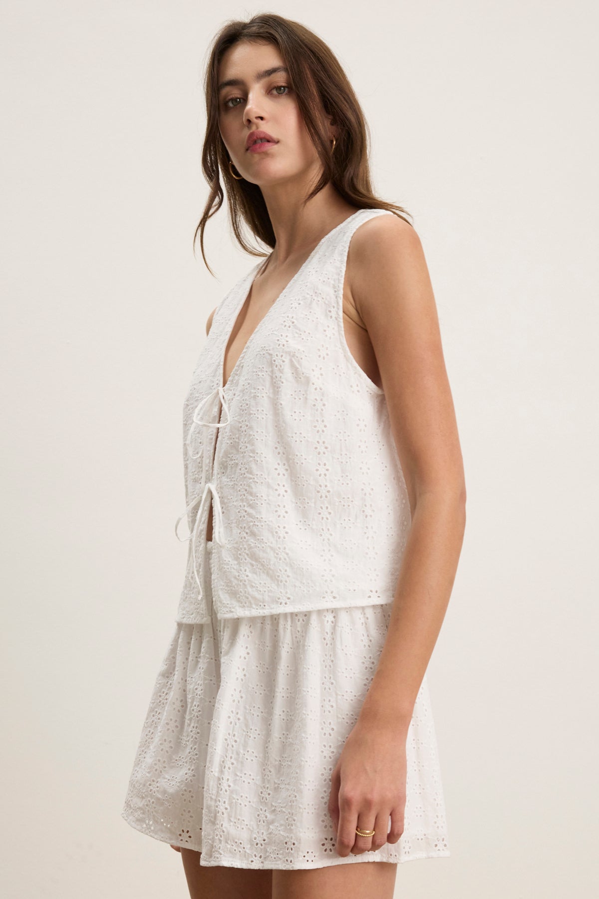 A woman wears the AVA EYELET TOP by Velvet by Graham & Spencer, a sleeveless, lightweight cotton top with a V-neck and tie details, standing against a plain background.-39123271024833