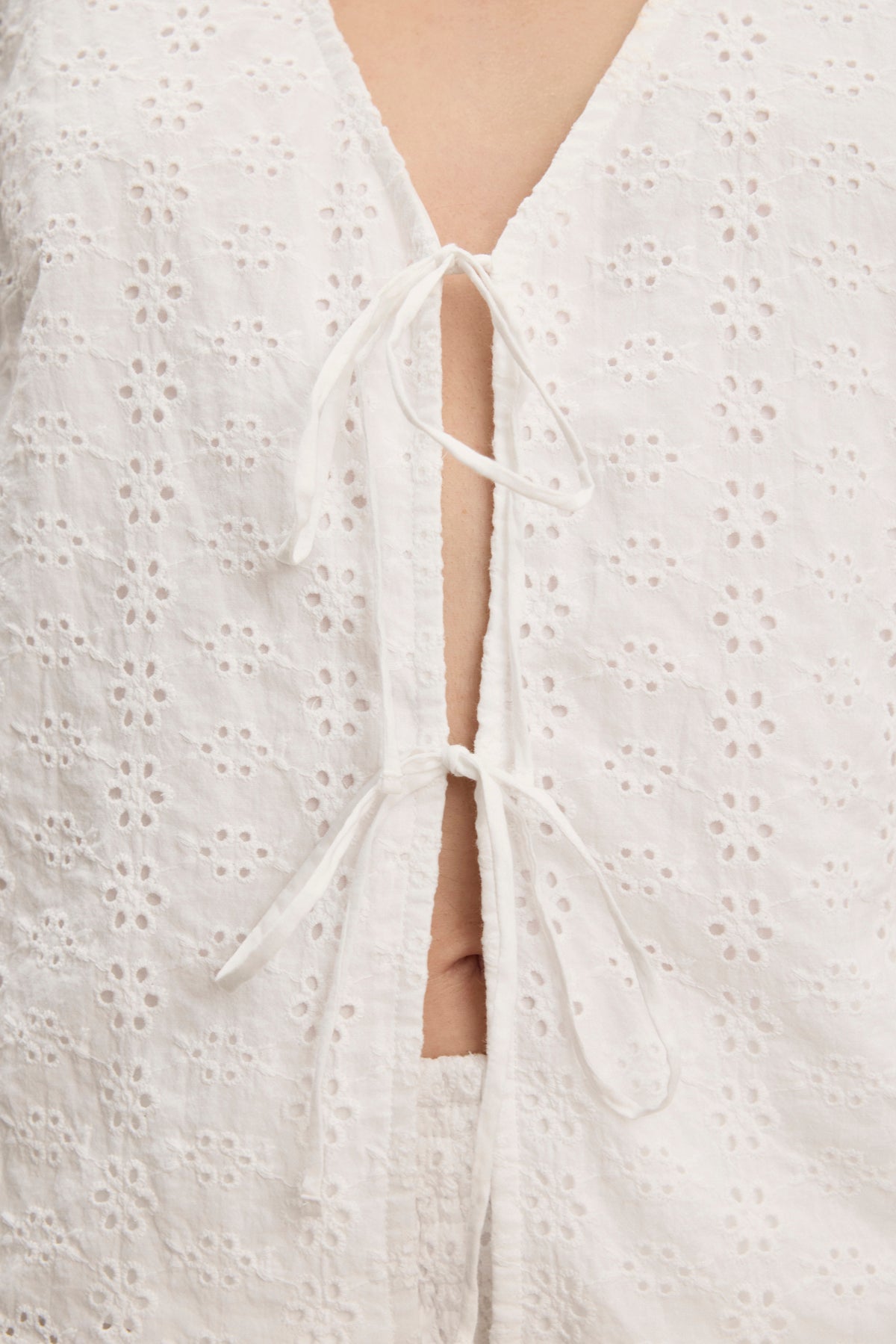 Close-up of the AVA EYELET TOP by Velvet by Graham & Spencer, featuring cotton eyelet fabric and two tied bows at the front—an elegant, feminine detail that lends versatility and charm to any wardrobe.