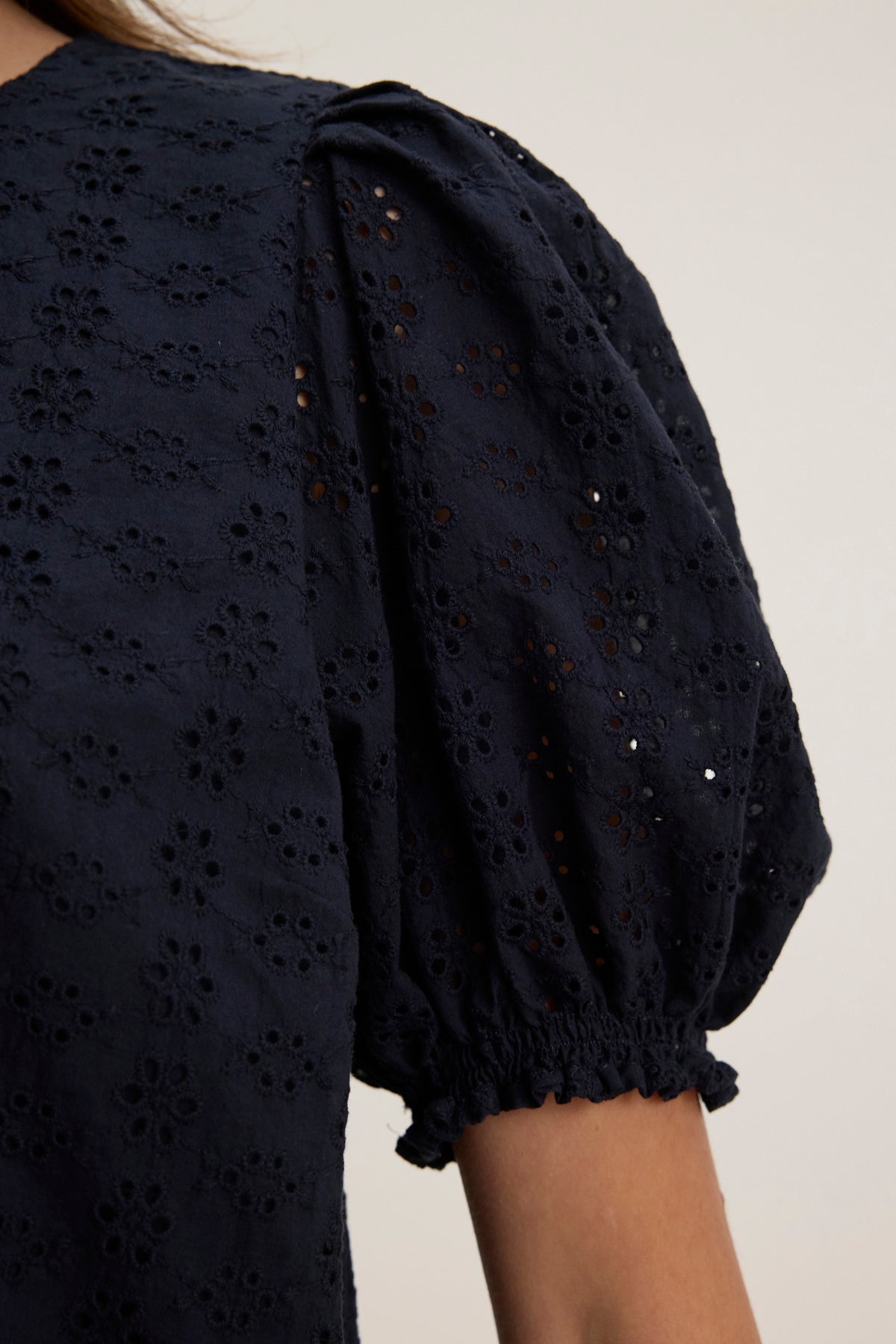 Close-up of the DALYN EYELET TOP by Velvet by Graham & Spencer, a dark blue cotton blouse with floral embroidery, gathered puff sleeves, and a back keyhole closure.-39123283771585