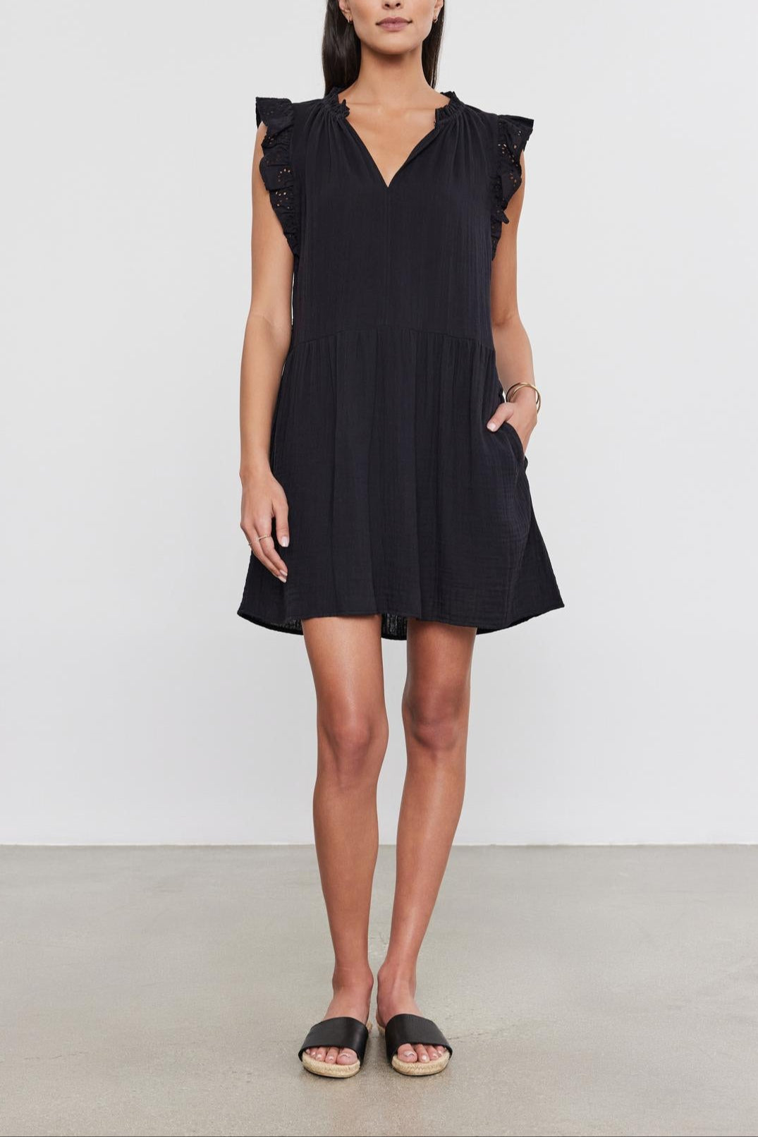 Woman in a black cotton gauze Grace dress by Velvet by Graham & Spencer with flutter sleeves, standing indoors, facing the camera with a neutral expression. She wears simple black sandals.-36910266187969