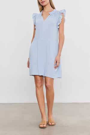 Woman in a Velvet by Graham & Spencer GRACE DRESS with puffy sleeves and sandals, standing against a plain background.