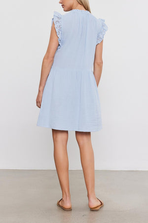 Woman standing facing away from the camera, wearing a Velvet by Graham & Spencer Grace Dress with lace shoulder details and sandals, on a plain background.