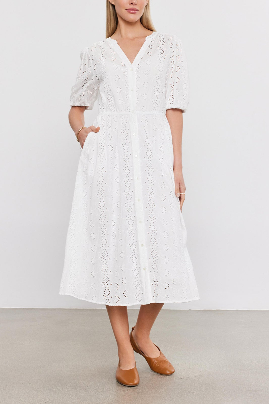 A woman stands in a studio wearing a white cotton eyelet midi dress with puff sleeves, paired with brown leather flats - the Velvet by Graham & Spencer RORI DRESS.-36910267924673
