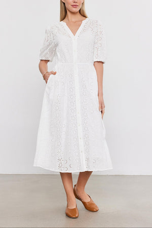 A woman stands in a studio wearing a white cotton eyelet midi dress with puff sleeves, paired with brown leather flats - the Velvet by Graham & Spencer RORI DRESS.