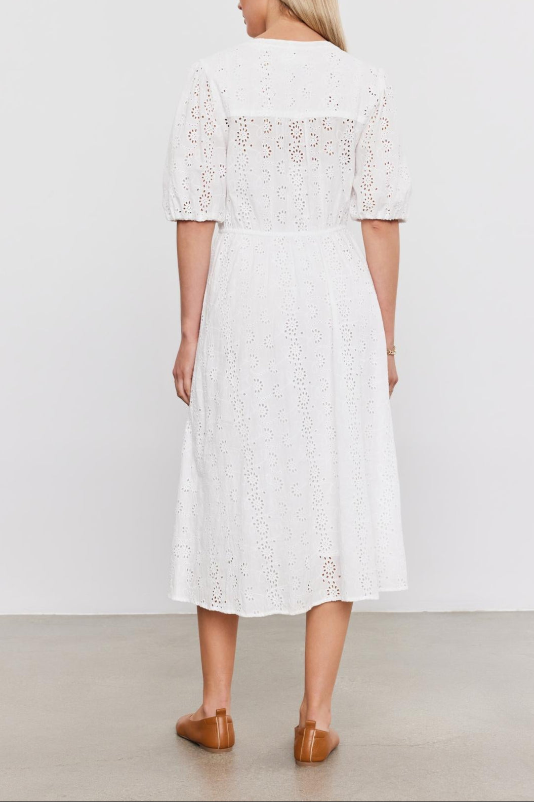 Woman in a white cotton eyelet mid-length RORI DRESS with puff sleeves, viewed from behind, standing against a plain background. She's wearing brown loafers by Velvet by Graham & Spencer.-36910267990209