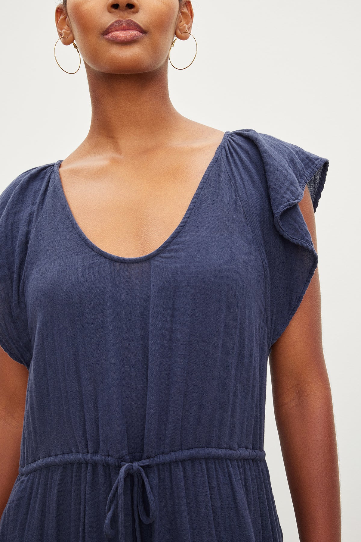 Close-up of a woman wearing a blue Adalyn cotton gauze tiered dress by Velvet by Graham & Spencer with short sleeves and a tie waist, focusing on the scoop neckline and shoulder detail.-35982554497217