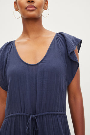 Close-up of a woman wearing a blue Adalyn cotton gauze tiered dress by Velvet by Graham & Spencer with short sleeves and a tie waist, focusing on the scoop neckline and shoulder detail.