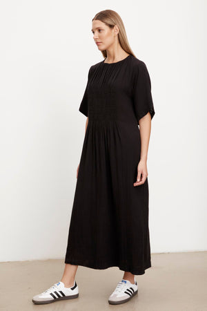 The model is wearing a Velvet by Graham & Spencer black ASHLEIGH COTTON GAUZE MAXI DRESS with pleats.