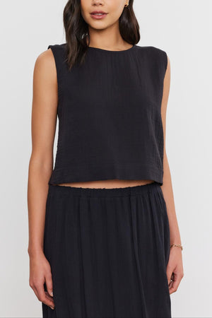 Woman wearing a sleeveless black Velvet by Graham & Spencer AUBREN COTTON GAUZE TANK TOP, standing against a plain background, with a faint smile.
