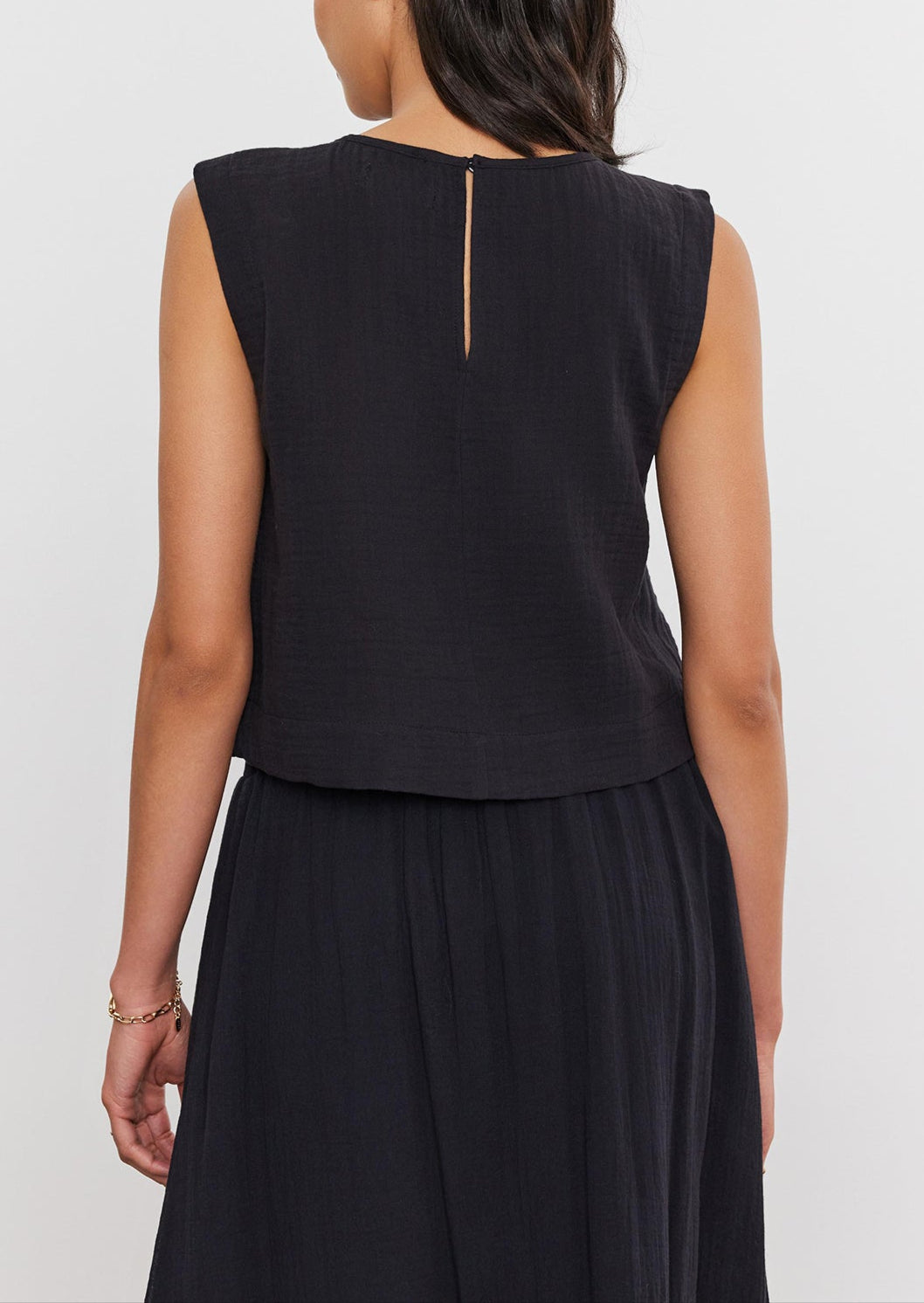 Rear view of a woman with medium-length hair wearing a sleeveless AUBREN COTTON GAUZE TANK TOP and matching skirt, standing against a white background by Velvet by Graham & Spencer.-36910090748097