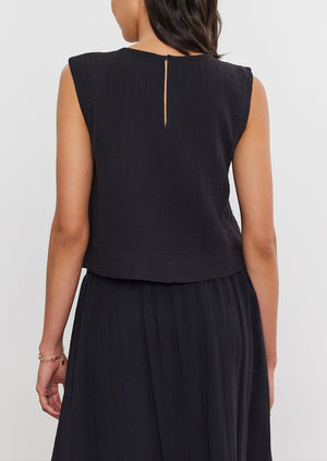 Rear view of a woman with medium-length hair wearing a sleeveless AUBREN COTTON GAUZE TANK TOP and matching skirt, standing against a white background by Velvet by Graham & Spencer.