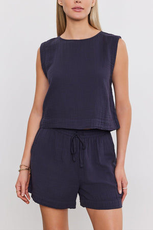 A person wearing a sleeveless navy AUBREN COTTON GAUZE TANK TOP by Velvet by Graham & Spencer and matching drawstring shorts, both crafted from airy cotton gauze, poses against a plain background.