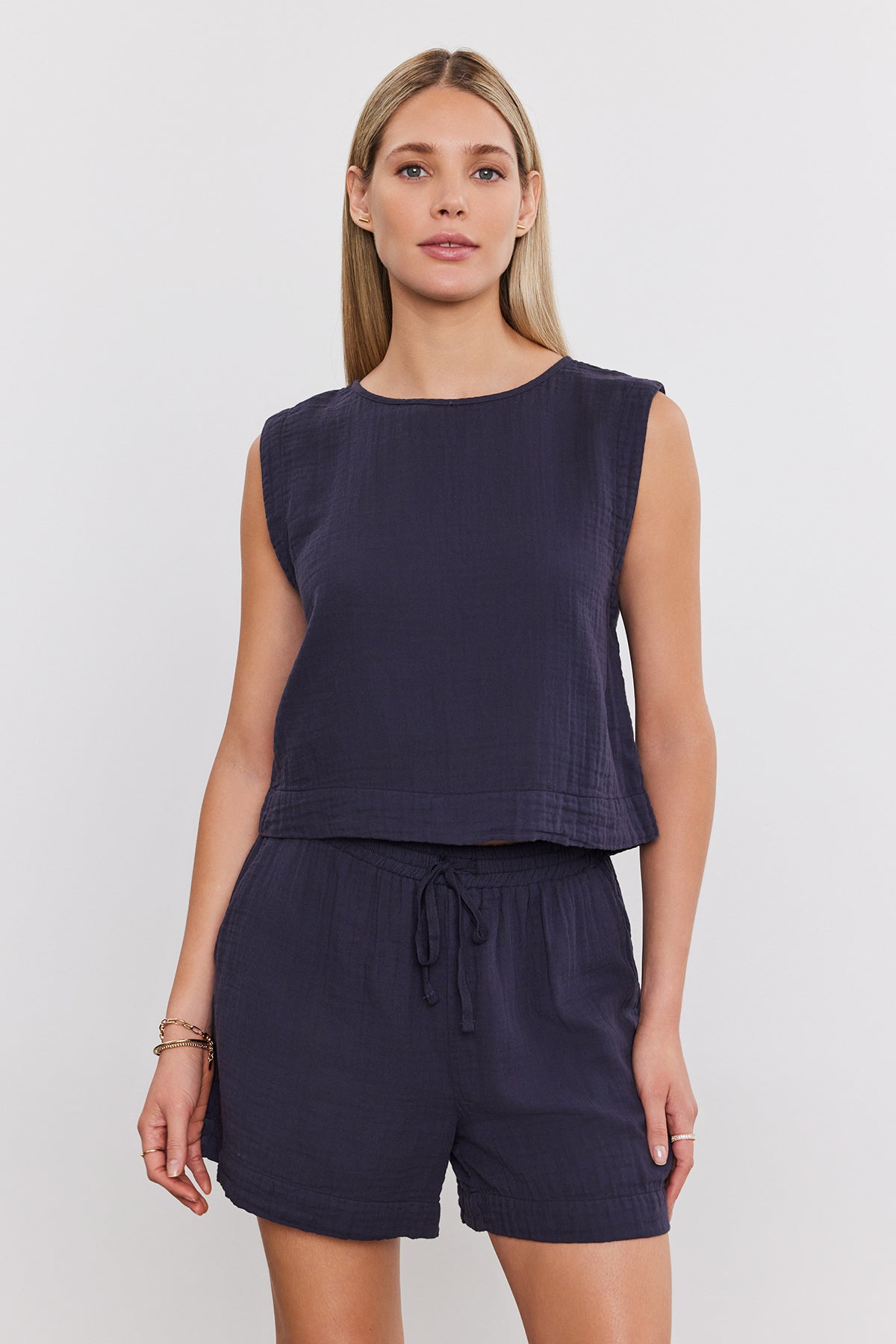 A woman with long hair is wearing a sleeveless navy top and matching Velvet by Graham & Spencer TIBBY COTTON GAUZE SHORT with a drawstring elasticized waist, standing against a plain white background.