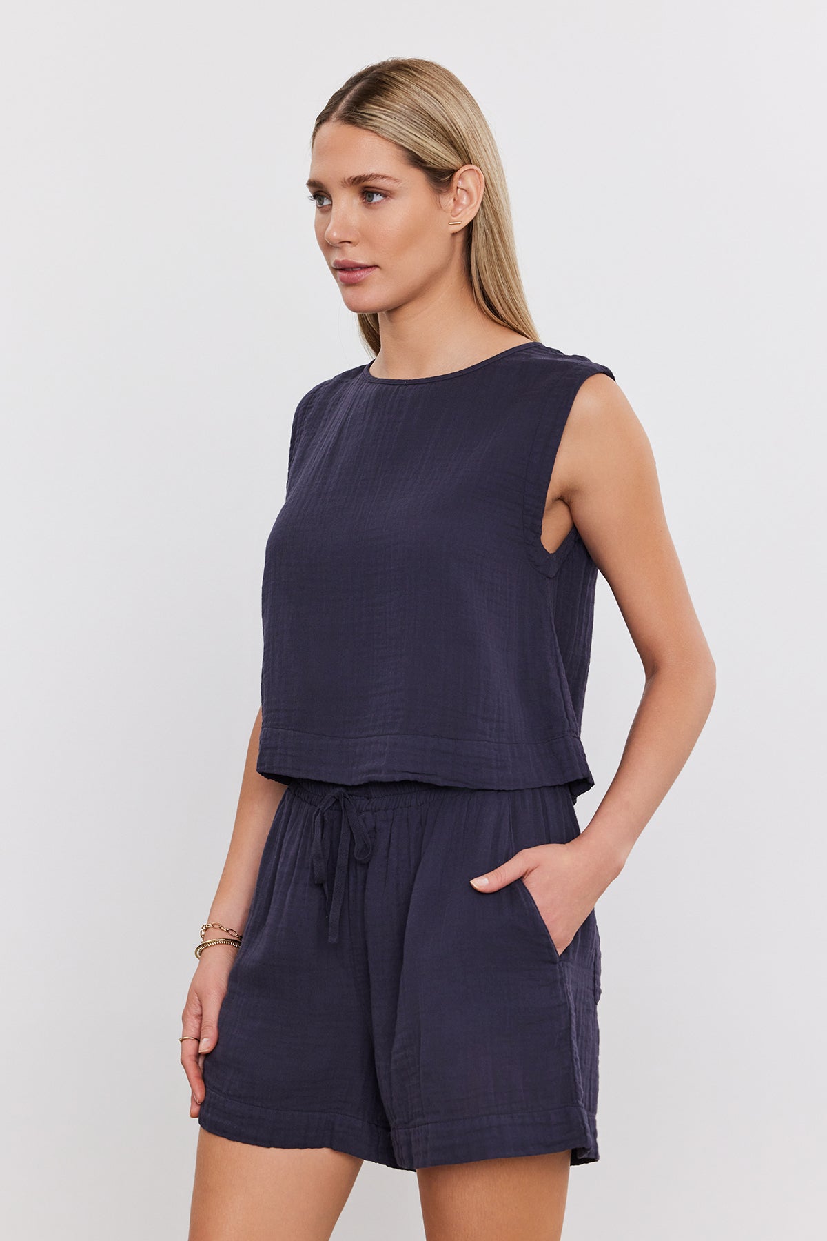 A woman wearing a sleeveless dark blue top and matching TIBBY COTTON GAUZE SHORT by Velvet by Graham & Spencer, hands in pockets, facing slightly to the side.-37452698222785