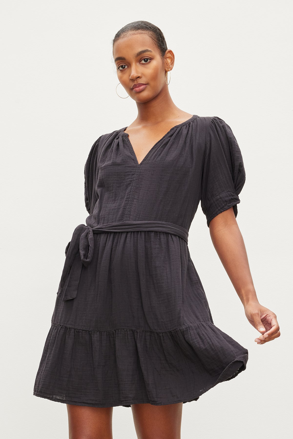 A woman in a Velvet by Graham & Spencer BELLA COTTON GAUZE DRESS with puff sleeves and a ruffled hem, standing against a light background.-35955428229313