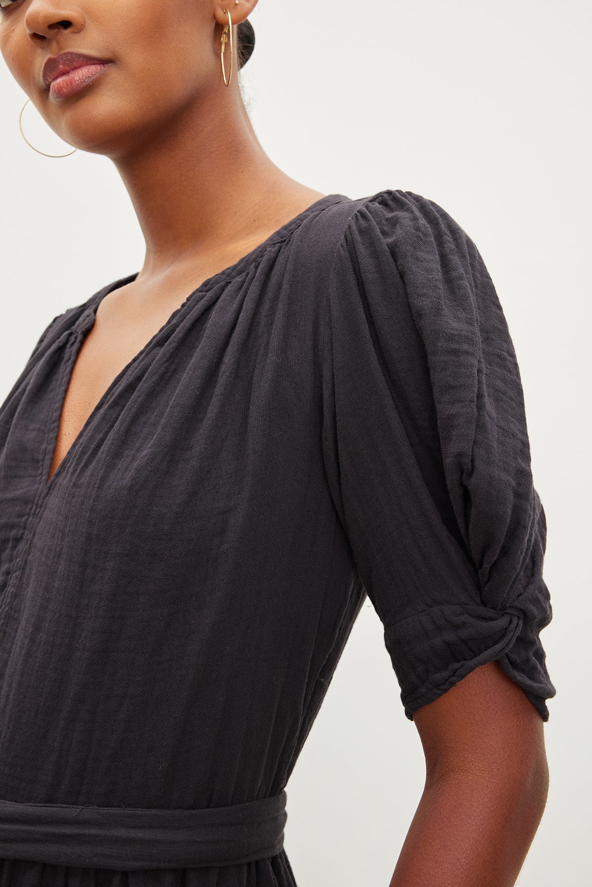 Close-up of a woman wearing a dark Velvet by Graham & Spencer dress, focusing on the puff sleeve detail, with a glimpse of her earring and profile.