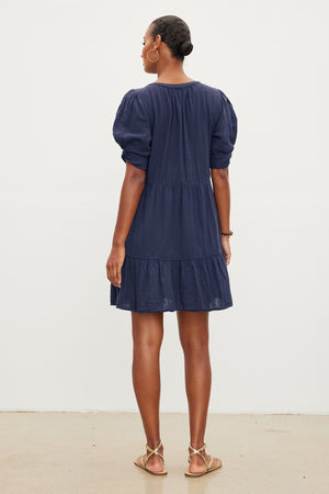 A person with short hair wearing a navy blue BELLA COTTON GAUZE DRESS by Velvet by Graham & Spencer and sandals is standing with their back to the camera against a plain white background.