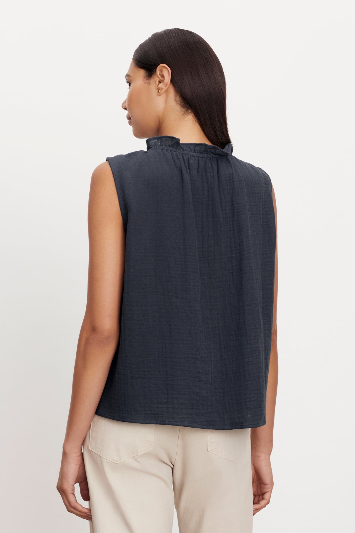 A person with long dark hair, wearing a Velvet by Graham & Spencer BIANCA COTTON GAUZE TANK TOP with ruffle detailing around the collar and beige pants, is photographed from the back.-36462878326977