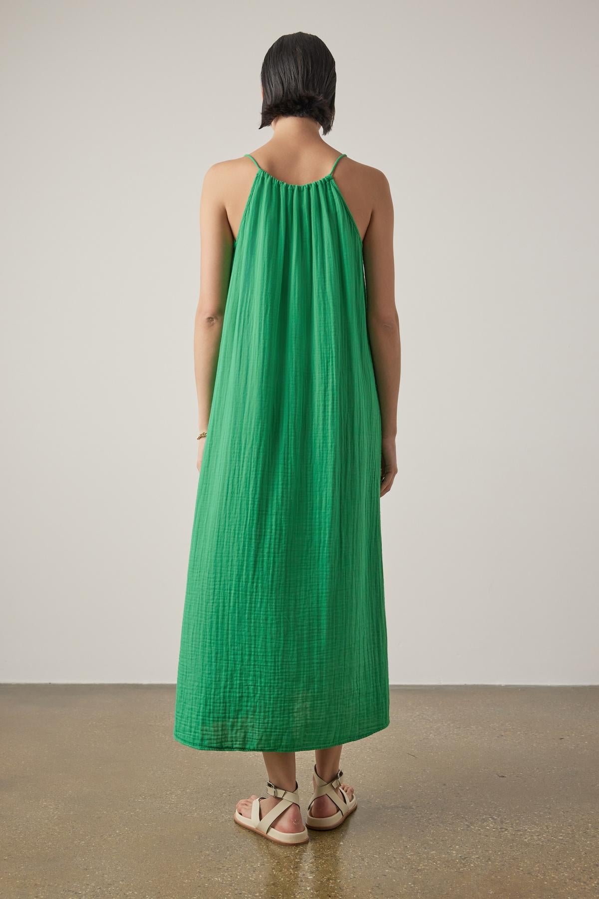 Woman standing with her back to the camera, wearing a green sleeveless CARRILLO DRESS by Velvet by Jenny Graham and white sandals, against a neutral background.-36863272157377