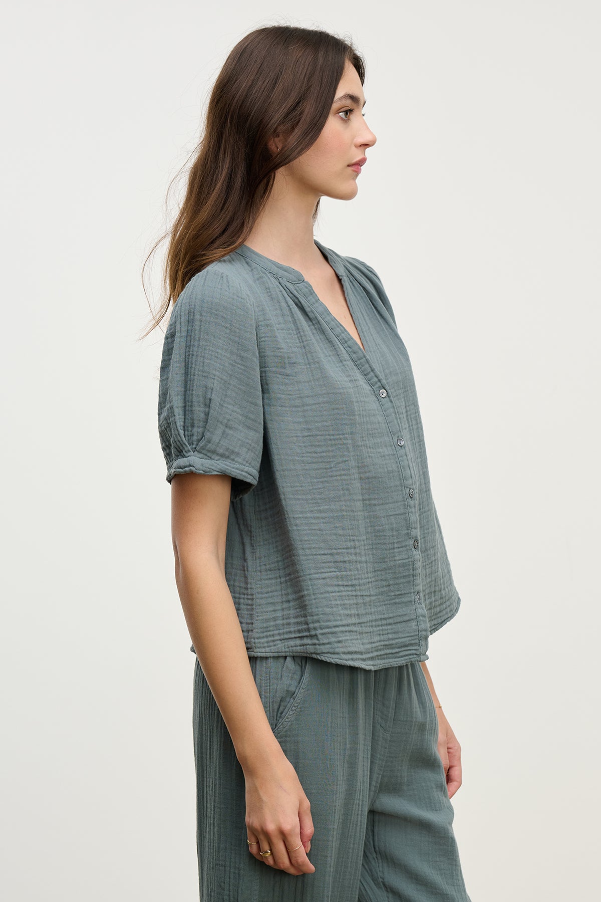 Person seen in profile wears the Velvet by Graham & Spencer DEANN COTTON GAUZE TOP—a loose-fitting, textured green top with a v-neckline—paired with matching cotton gauze pants.-38662568247489