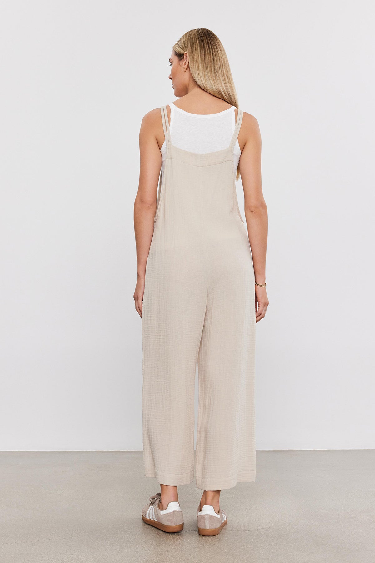 Woman standing facing away, wearing a Velvet by Graham & Spencer EVERLEE COTTON GAUZE JUMPSUIT with wide legs and white sandals on a plain background.