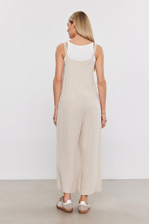 Woman standing facing away, wearing a Velvet by Graham & Spencer EVERLEE COTTON GAUZE JUMPSUIT with wide legs and white sandals on a plain background.