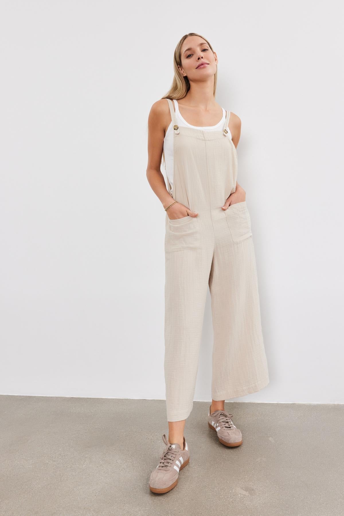 A young woman stands confidently, wearing a Velvet by Graham & Spencer EVERLEE COTTON GAUZE JUMPSUIT with sneakers, against a plain white backdrop.